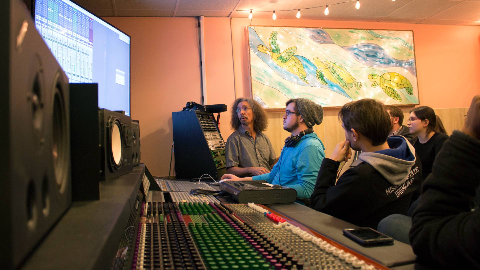Recording arts students gather around screen and sound board